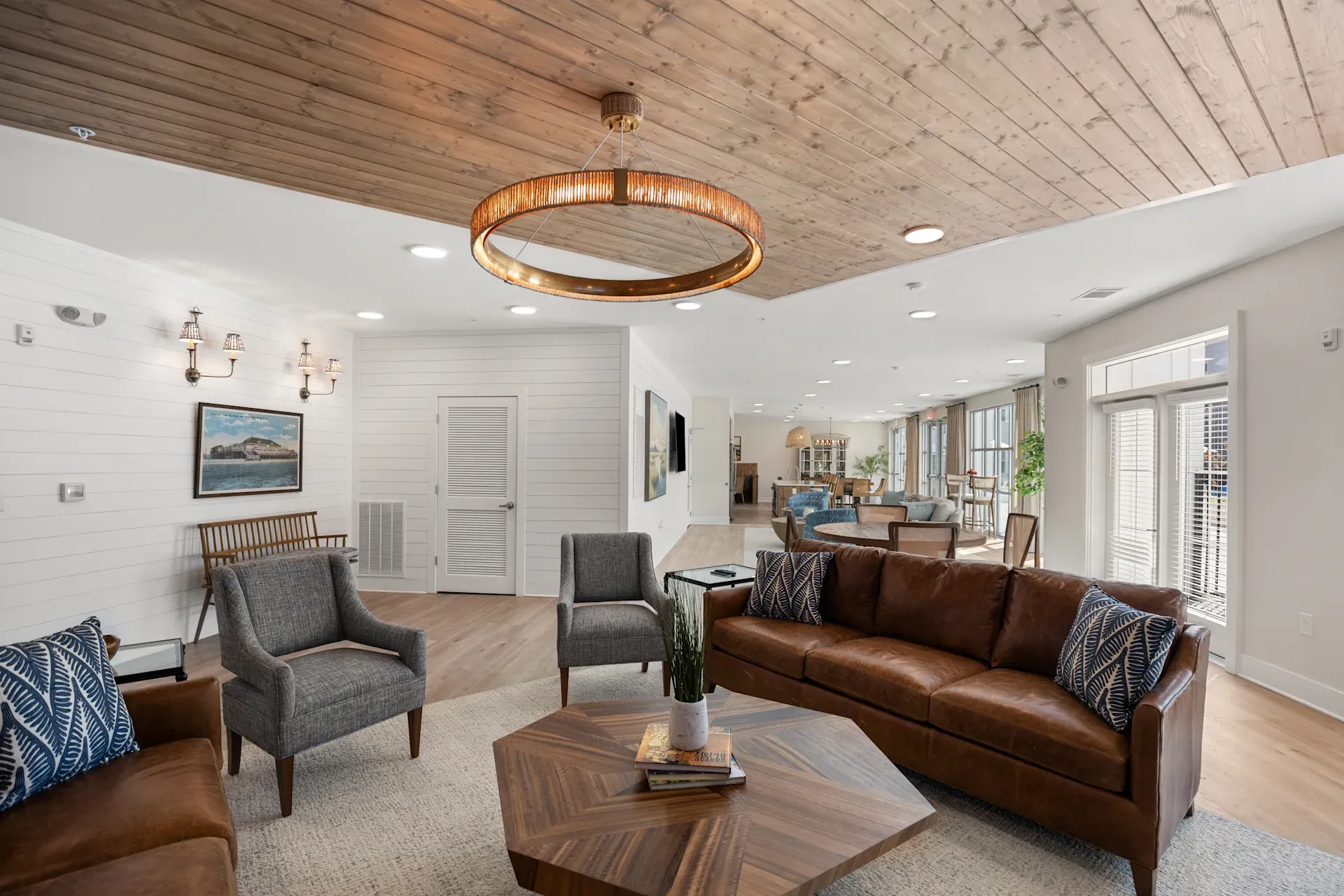 Modern lounge with leather sofa, gray chairs, wood ceiling, coffee table, and large windows letting in light.