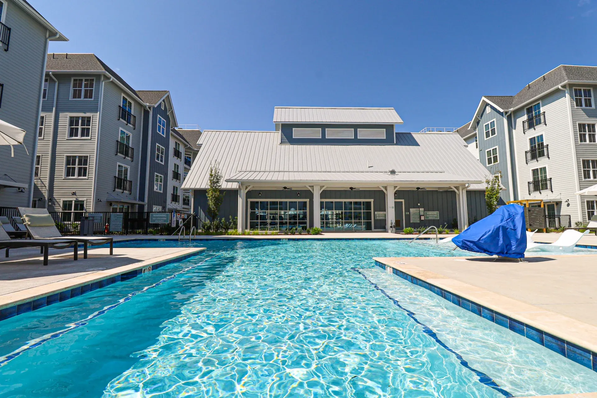 Outdoor swimming pool surrounded by modern apartment buildings under a clear blue sky.