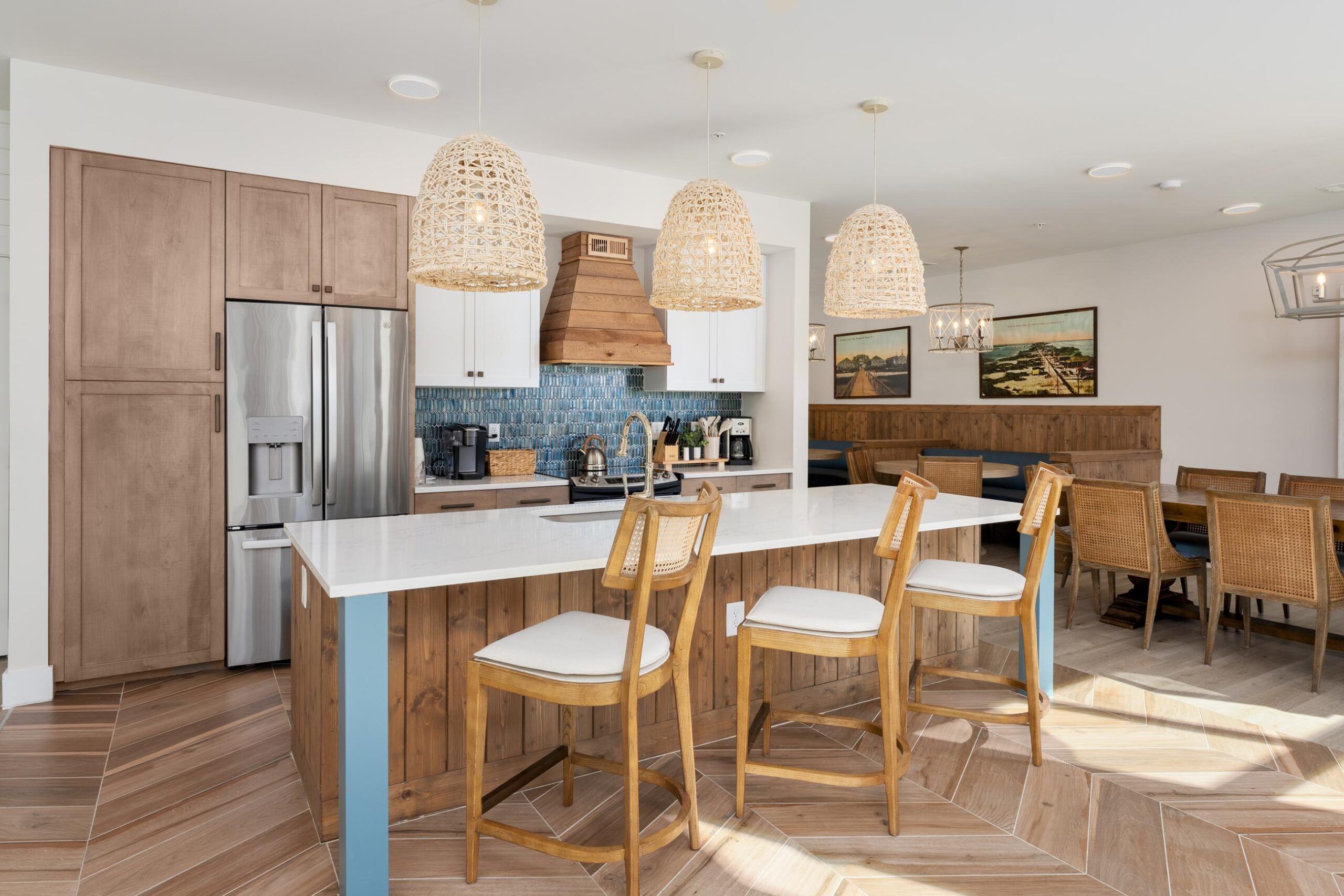 Modern kitchen with wooden cabinets, blue tile backsplash, island with chairs, and woven pendant lights.
